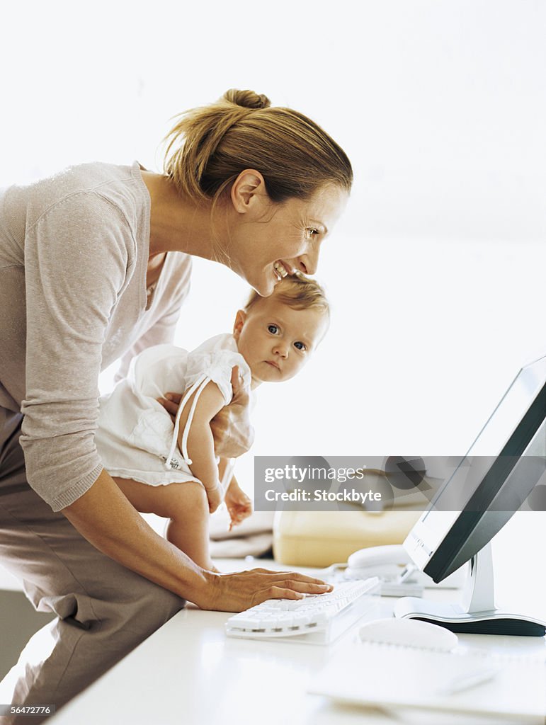 Side profile of a businesswoman carrying her daughter and using a computer