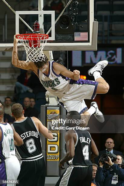 Andrew Bogut of the Milwaukee Bucks hangs from the rim after a dunk as Rasho Nesterovic and Michael Finley of the San Antonio Spurs look on on...