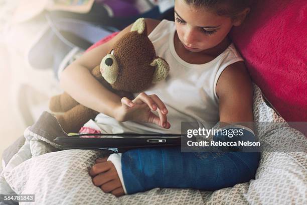 girl, with broken arm, using tablet in bed - orthopaedic equipment imagens e fotografias de stock