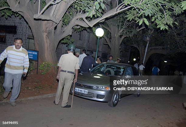 Indian security personnel stand guard near a car that was damaged after a gunman opened fire on the campus of the Indian Institute of Science campus...