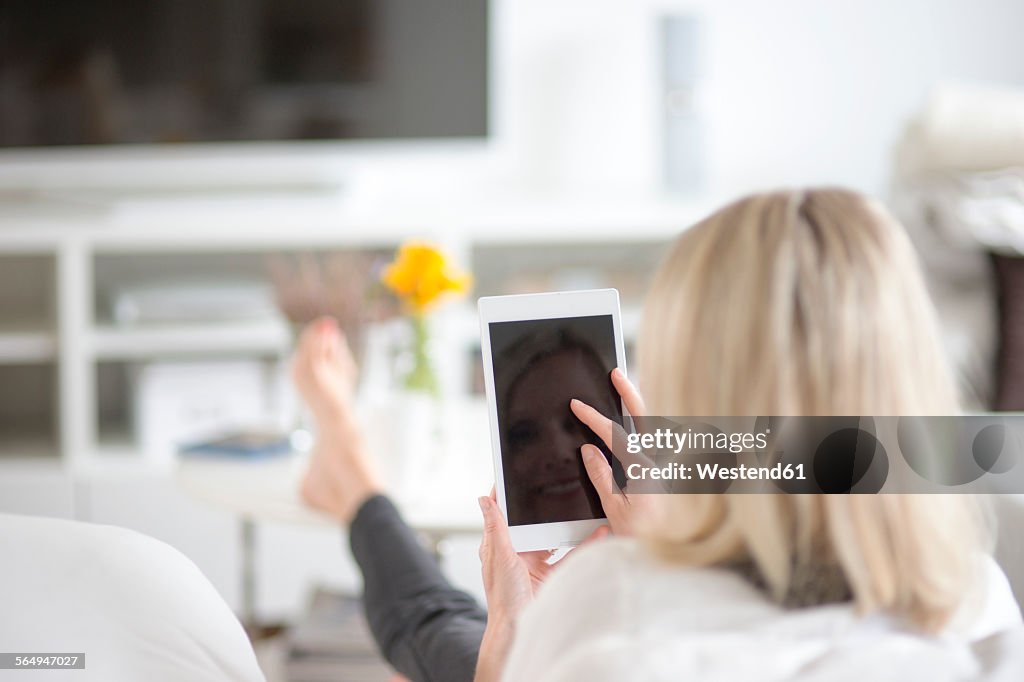 Back view of blond woman using mini tablet at home