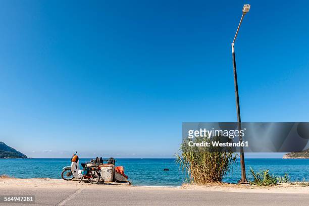 greece, corfu, agios georgios, moped and street lamp at the ocean - roadside stock-fotos und bilder