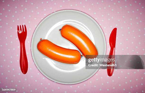 plate with two pork sausages and red plastic cutlery on pink cloth - baloney stock pictures, royalty-free photos & images