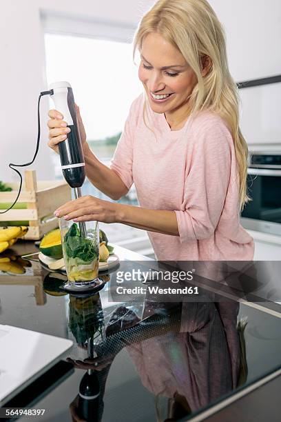 smiling young woman preparing smoothie in the kitchen - blender stock-fotos und bilder