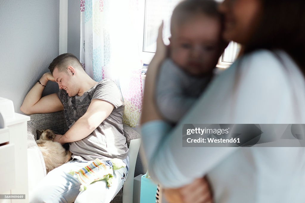 Mother holding baby and father petting cat at home