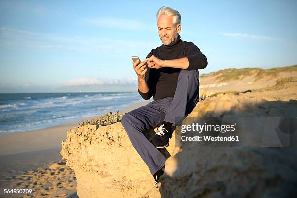 south africa, portrait of man sitting on a rock at the beach using smartphone - 50 sombras fotografías e imágenes de stock