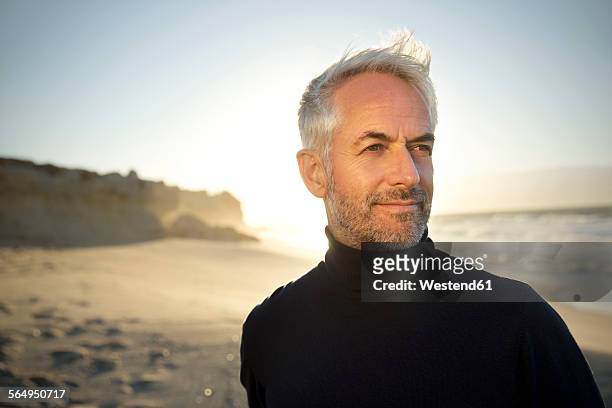 south africa, portrait of white haired man wearing turtleneck standing on the beach before sunrise - mirada de reojo fotografías e imágenes de stock