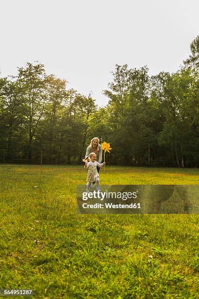 mother and daughter running with paper windmill on meadow - windrad natur wiese stock-fotos und bilder