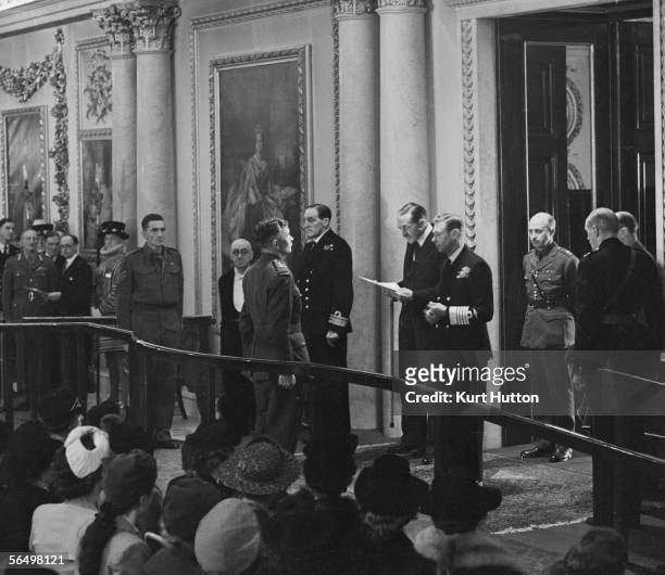 Captain Charles Upham stands before King George VI at Buckingham Palace, London, during a Royal Investiture ceremony, 7th April 1945. His citation is...
