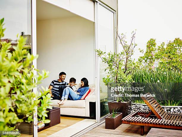 smiling family on sofa looking at digital tablet - modern apartment exterior stock-fotos und bilder