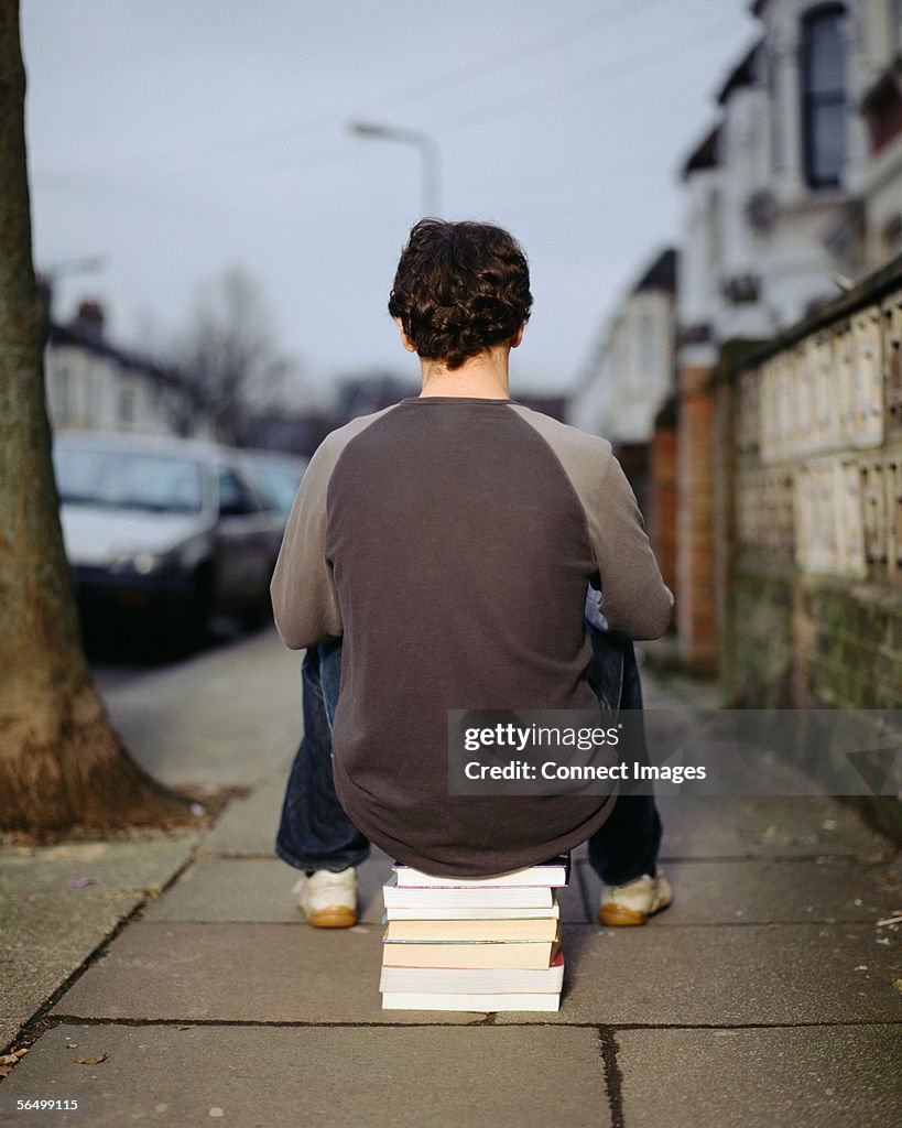 A young man sitting on a pile of books