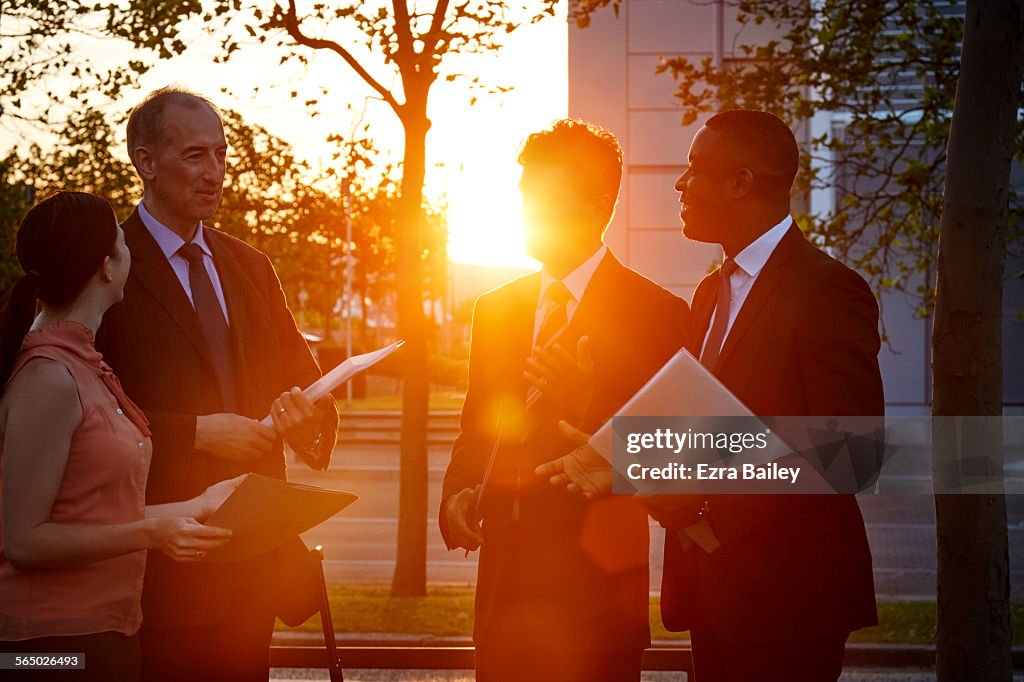 Colleagues chat outside an office during a sunset