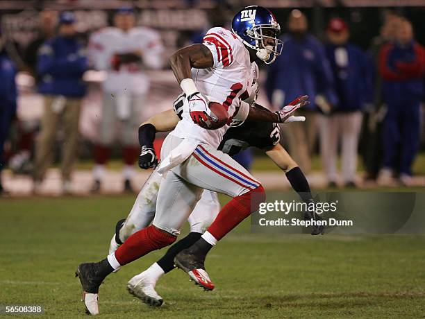 Plaxico Burress of the New York Giants runs with the ball against Stuart Schweigert of the Oakland Raiders and scores a touchdown on December 31,...