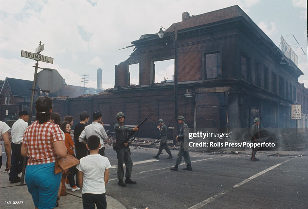 Bystanders observe National Guardsmen, armed with rifles standing ...
