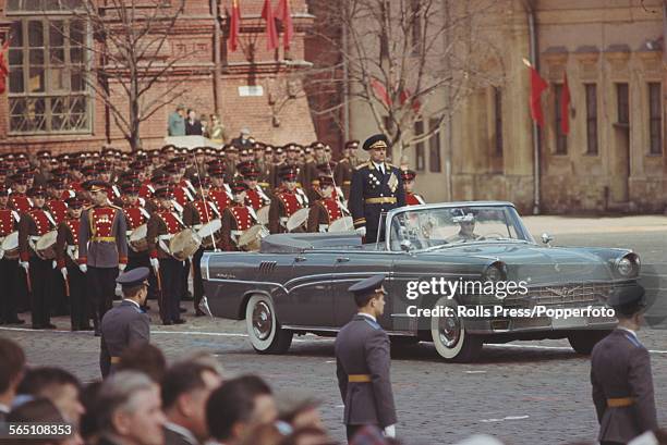 View of a Soviet general standing to attention in the rear passenger area of a ZiL-111V convertible limousine making up part of a May Day parade in...