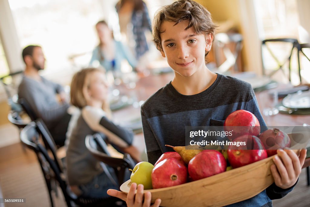 A boy caring a wooden tray of apples.