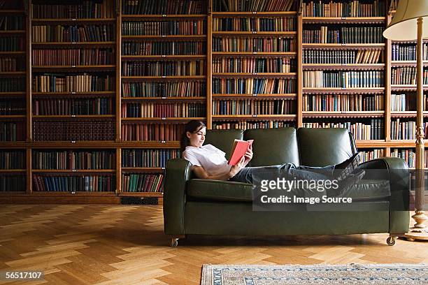 femme lisant sur un canapé dans la bibliothèque - bookshelf photos et images de collection