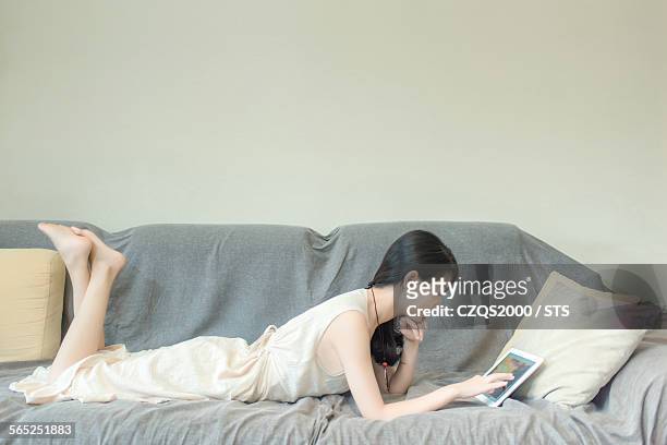 young woman using digital tablet on sofa at home - pés cruzados - fotografias e filmes do acervo