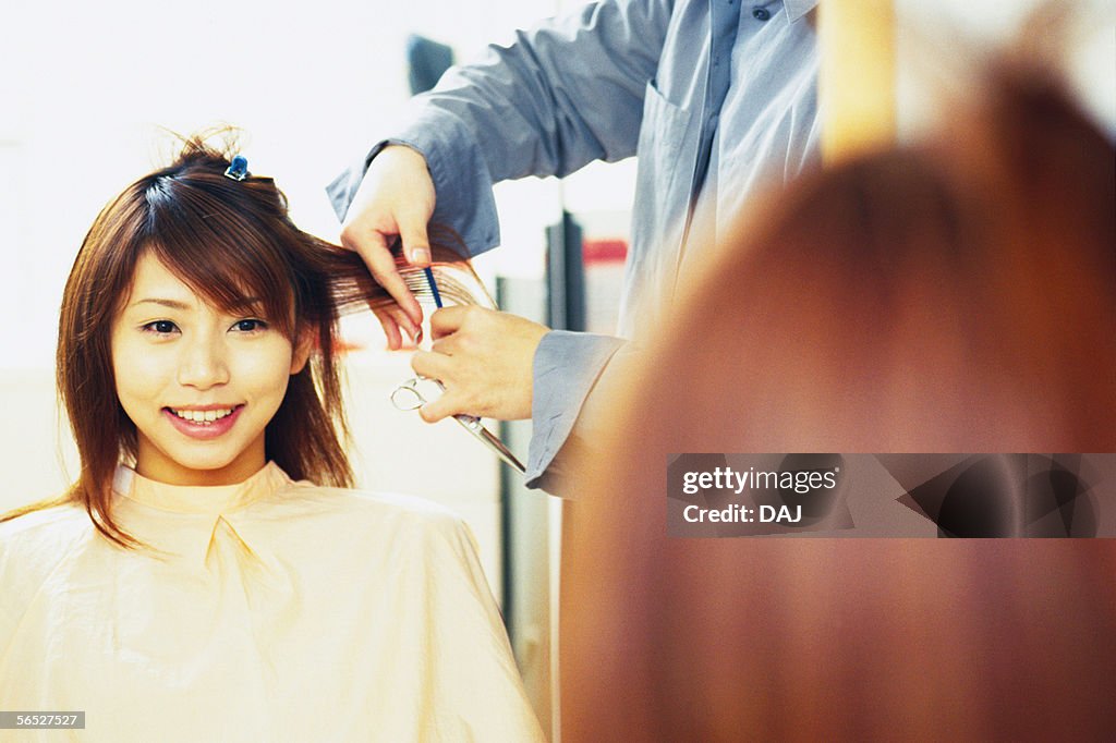 Hairdresser cutting young woman's hair with Scissors