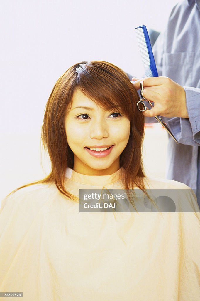 Hairdresser cutting young woman's hair with Scissors