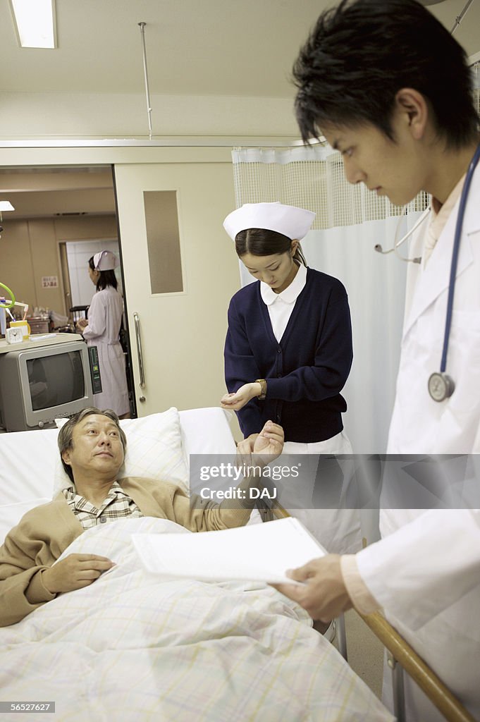 Nurse takes the pulse of a patient lying in a hospital bed