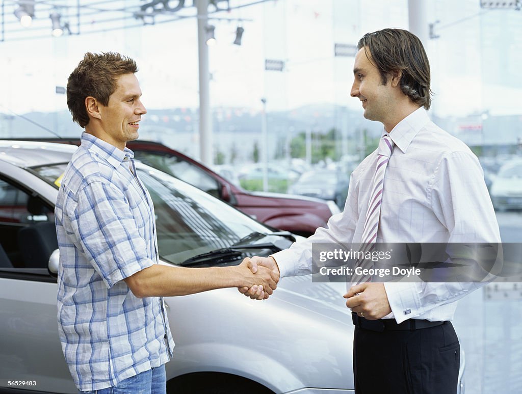 Side profile of a young man shaking hands with a car dealer
