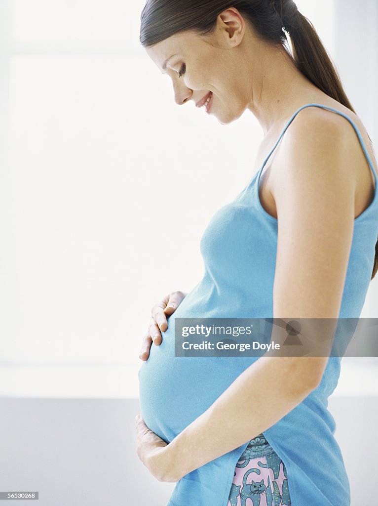 Side profile of a pregnant woman touching her abdomen