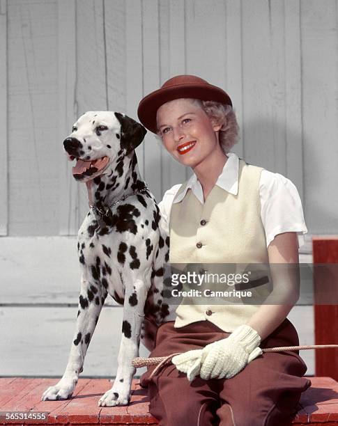 Portrait of a young woman in riding outfit posing with her Dalmatian dog, Los Angeles, California, 1950.