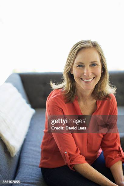 portrait of smiling woman sitting on sofa - 40 year old woman blonde blue eyes stock pictures, royalty-free photos & images