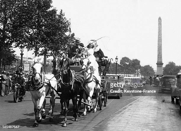 Un homme avec chapeau haut-de-forme assis à côté d'une femme en robe longue dans une voiture hippomobile tirée par quatre chevaux, place de la...
