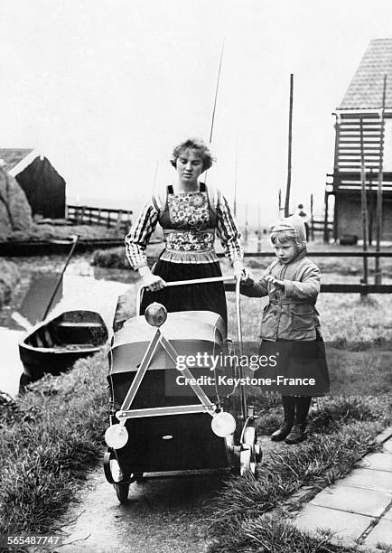 Près d'une rivière, une femme en tenue traditionnelle et accompagnée d'une petite fille derrière une poussette équipée d'un triangle réfléchissant et...