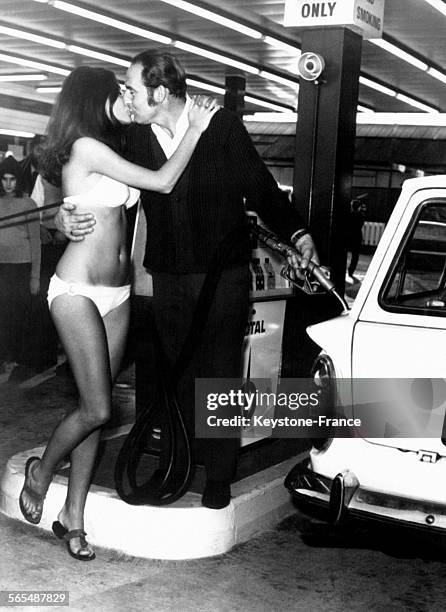 Jeune femme en bikini embrassant un client dans une station essence, à Londres, Angleterre, Royaume-Uni, le 12 octobre 1970.