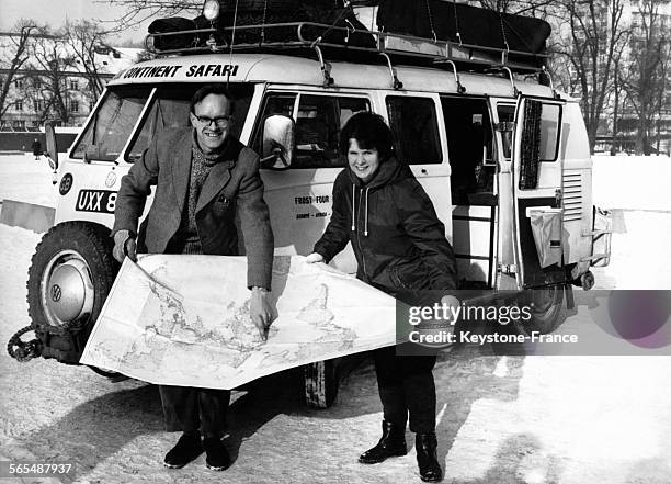 Côté de leur minivan combi Volkswagen, David et Christina Frost, couple de jeunes journalistes anglais, devant une carte routière en train de montrer...