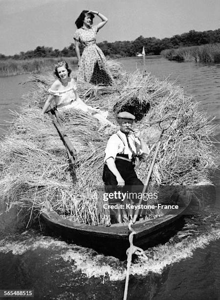 Sur une rivière, deux femmes sont sur une botte de foin qu'un paysan transporte sur son bateau, à Ranworth, Royaume-Uni le 30 juin 1949.
