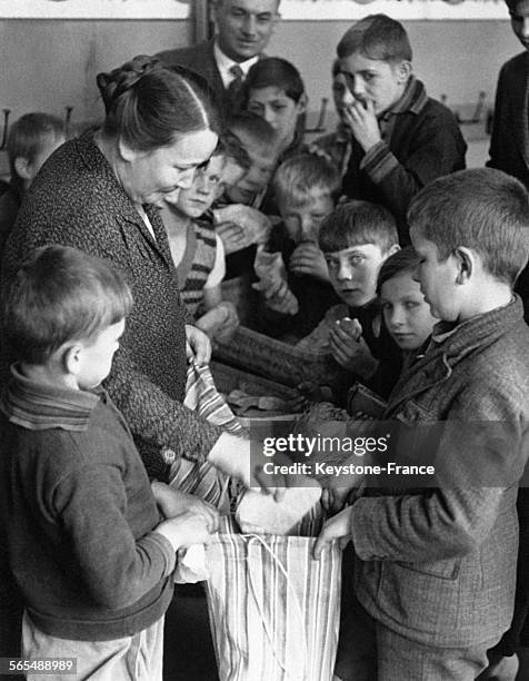 Une femme place des sandwiches dans le sac en tissu que lui tend un jeune garçon assisté du reste de la classe.