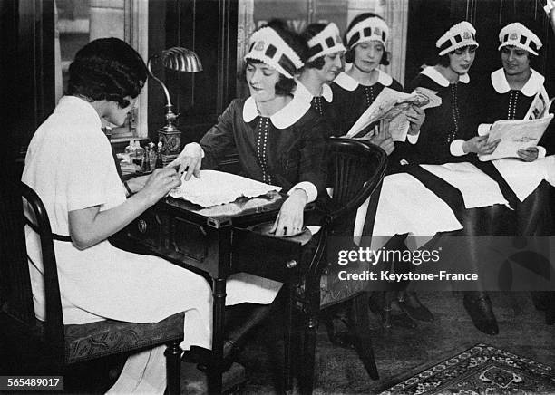 Une femme de chambre se fait faire les ongles par une manucuriste pendant que ses compagnes patientent en feuilletant des magazines.