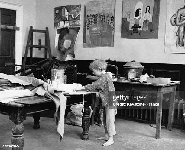 Un petit garçon met du désordre sur une table de travail dans un studio de peinture.