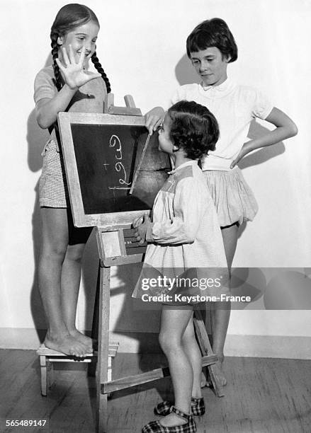 Un petit garçon de cinq ans apprend à effectuer une addition au tableau noir avec l'aide de deux camarades le 12 septembre 1959.