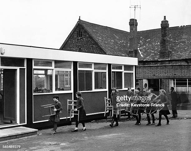 Des élèves d'une école primaire déménagent les chaises de leur classe vers le nouveau bâtiment le 13 janvier 1966 à Coventry, Royaume-Uni.