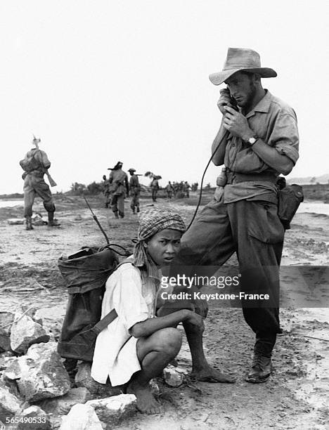 Un caporal chef, debout à côté d'un jeune garçon assis portant le sac à dos contenant le matériel de communication, parle dans le combiné, dans la...