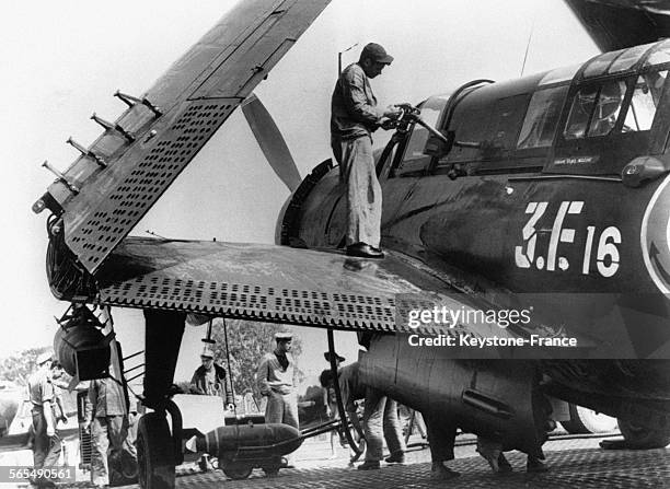 Un homme remplit de carburant un Helldiver de l'aéronavale, ailes repliées, sur le pont du porte-avions 'Arromanches', le 10 avril 1954.