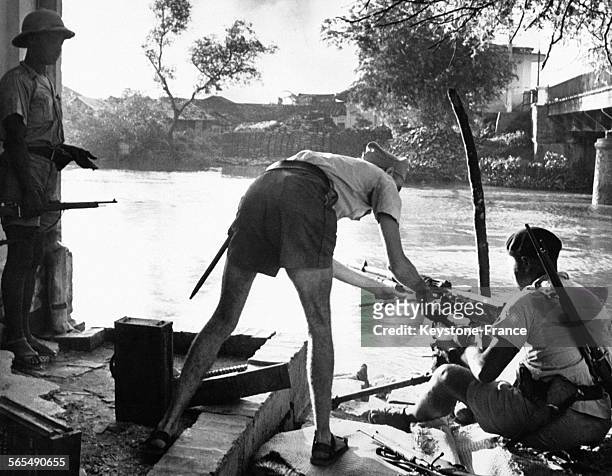 Soldat français mettant des munitions dans le fusil-mitrailleur d'un combattant civil, au bord d'un fleuve, à Saigon, Viêt Nam, le 17 octobre 1945.