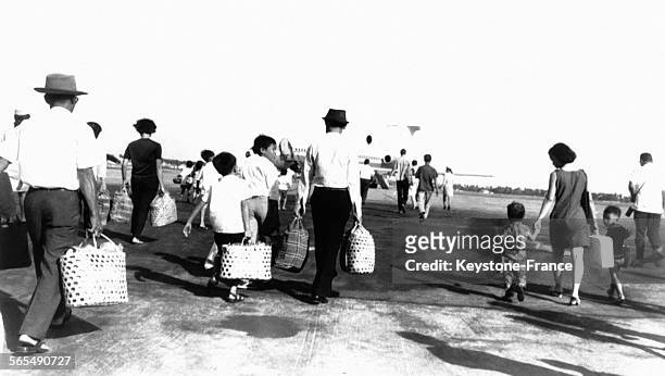 Sur la piste de l'aéroport de Pochengtong, hommes, femmes et enfants, avec valises et sacs à la main, se dirigent vers l'avion, à Phnom Penh, au...