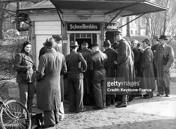 Hommes et femmes attendant un snack dans une échoppe d'un parc de Hambourg, en Allemagne, en novembre 1945.