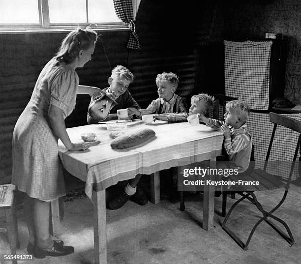 Une femme sert un chocolat à ses garçons assis autour de la table de la nouvelle laison préfabriquée, à Berlin, Allemagne, le 2 septembre 1946.