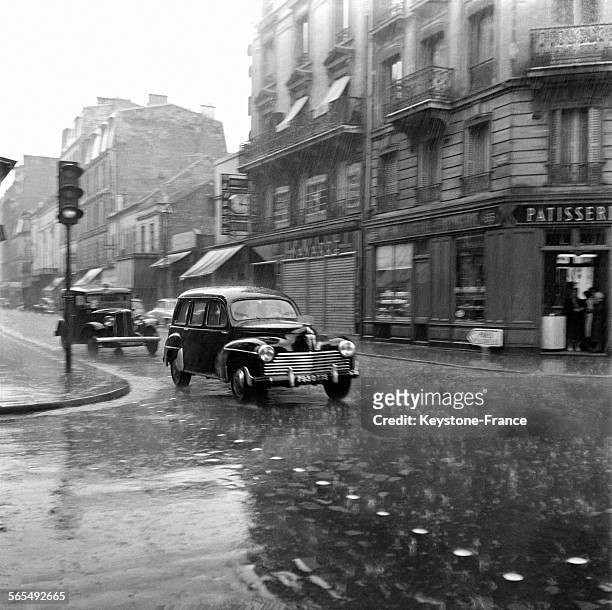 Une Peugeot 203 familiale roule sous les grêlons, devant un passage clouté, dans les rues de Levallois-Perret, France, le 9 juillet 1956.