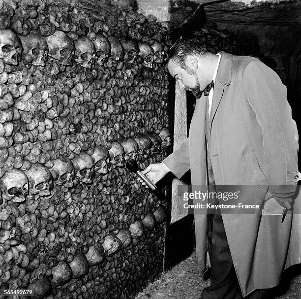 Bloc-notes et stylo à la main, un homme éclaire à la lampe de poche un crâne dans une des allées de la crypte-ossuaire des Catacombes de Paris,...