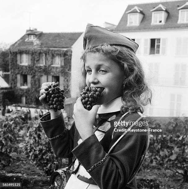 Fille en costume folklorique mange une grappe de raisin pendant la fête des vendanges à Montmartre, Paris, France le 28 septembre 1961.
