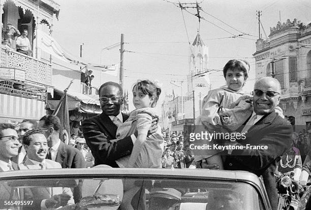 Au cours de la traversée de la capitale, les Présidents Senghor, à gauche et Bourguiba à droite, dans leur voiture, tiennent dans leurs bras deux...