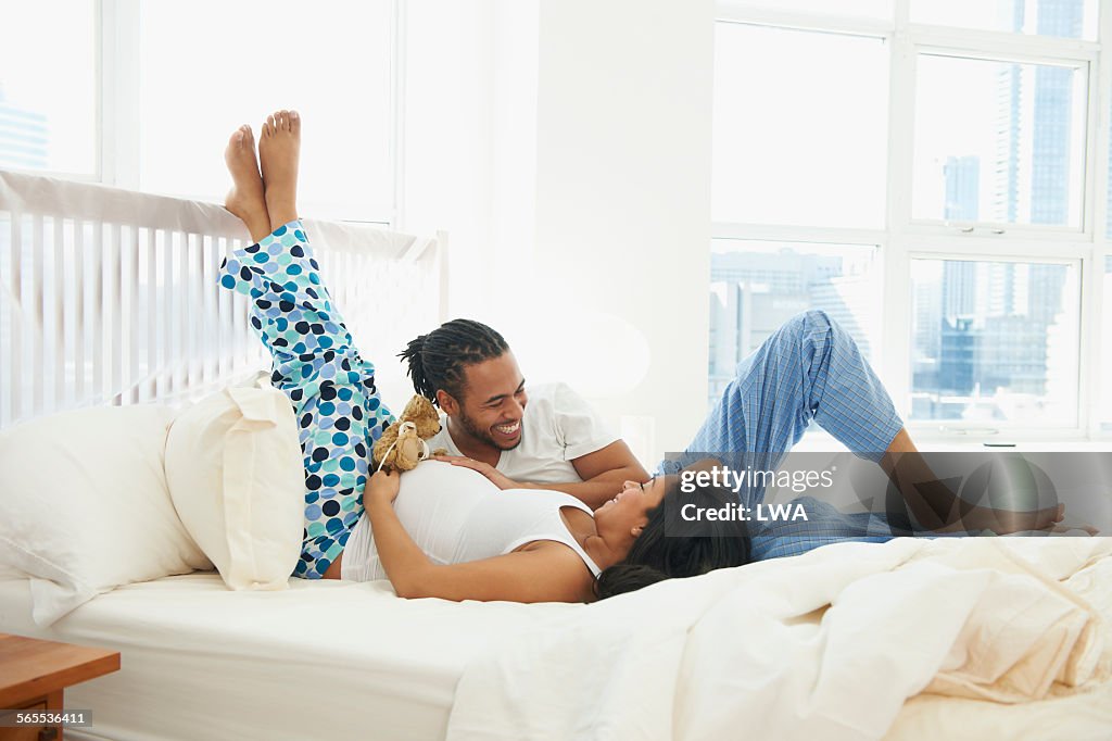 Husband laughing with pregnant wife in bed